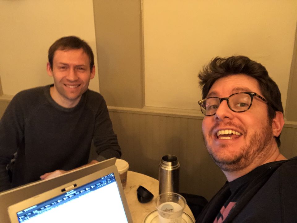 Dmitri and Marty sit around a small circular table with their laptops, smiling for the camera