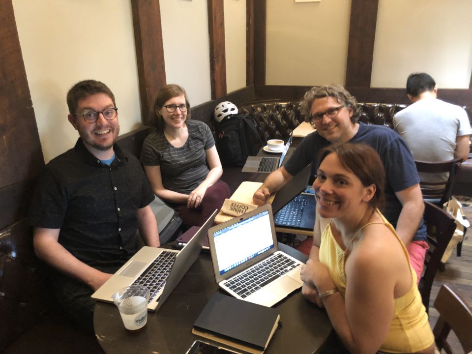 Marty, Amy, Matt, and Tiara grin at the camera, sitting around a table full of laptops