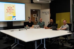 Four people sit at a conference table in a modern meeting room called "digital lab wg.110," with laptops and a large screen displaying the cover of "Das Web-Adressbuch fΓΌr Deutschland 2019."