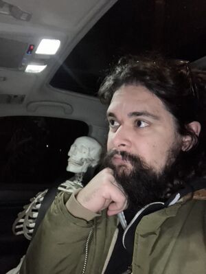 Isaac sits in a car with a skeleton in the passenger seat