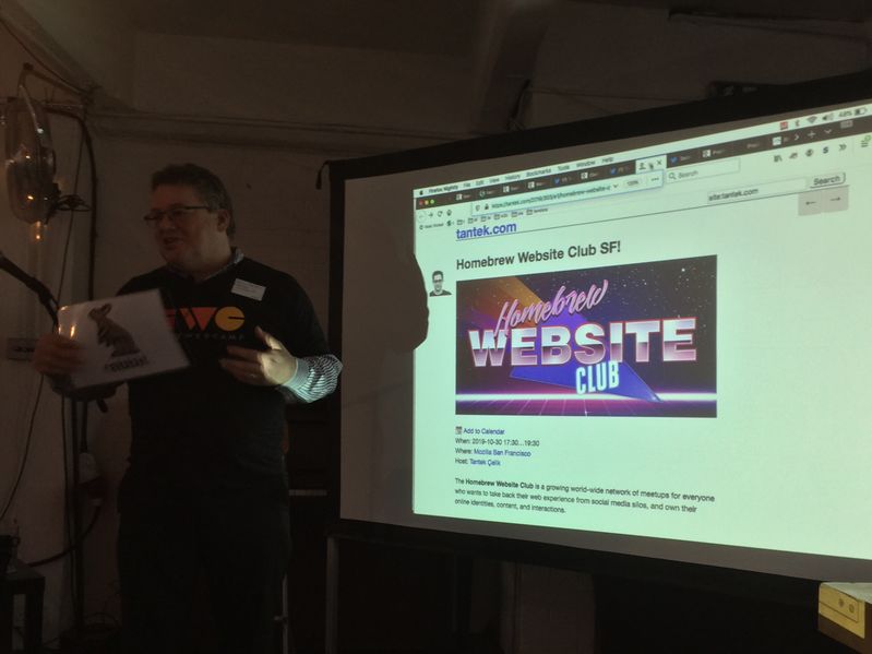 Kevin Marks wearing an IndieWebCamp t-shirt leading a discussion session with a projector screen next to him showing an indie event for Homebrew Website Club